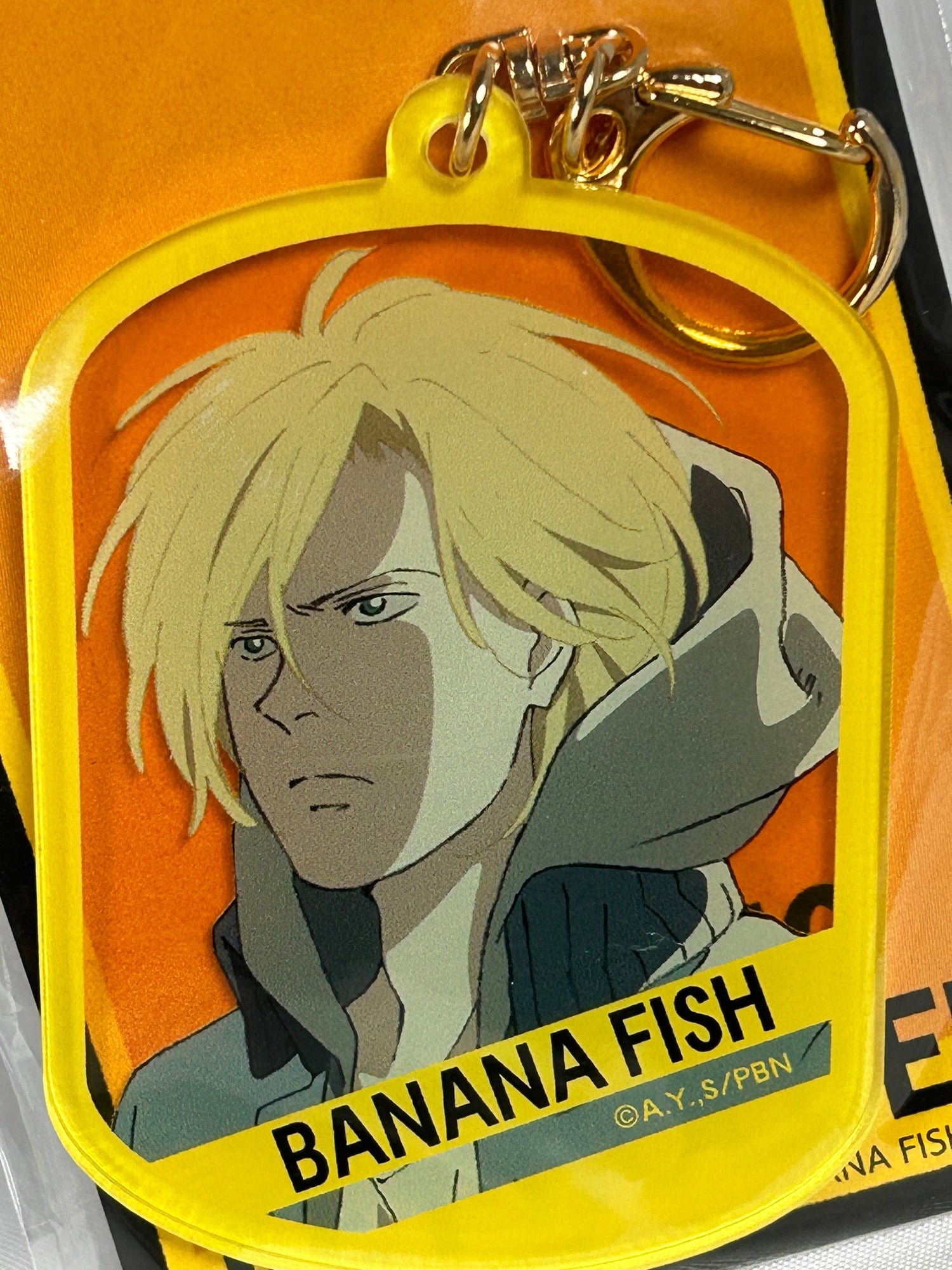 Ash lynx from Banana Fish wearing a hoodie on a yellow acrylic keychain for the Banana Fish Collection Page